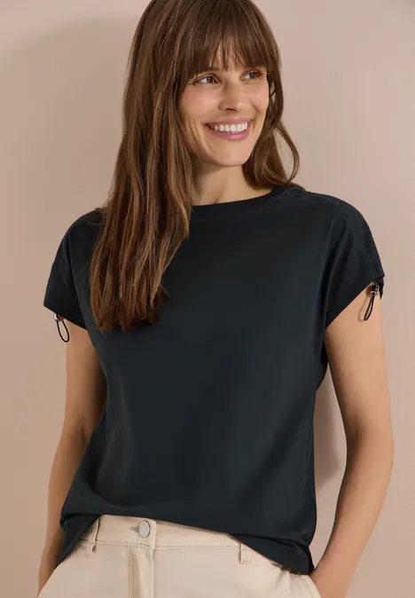 T-Shirt mit Raffung in Unifarbe palm breeze green Eine Frau trägt ein schwarzes T-Shirt und eine beigefarbene Hose vor neutralem Hintergrund.
