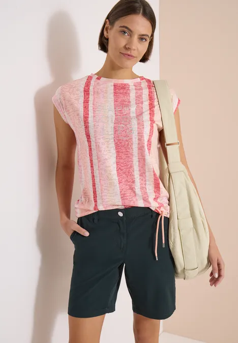 Frau in rosé-weiß gestreiftem T-Shirt, dunkelblauen Shorts und Schultertasche.