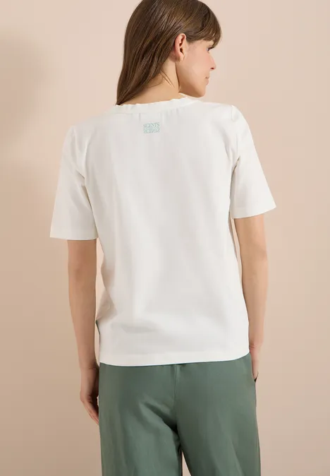 T-Shirt mit Rundhals und Brusttasche vanilla white Frau von hinten, trägt weißes T-Shirt und grüne Hose vor beigem Hintergrund.
