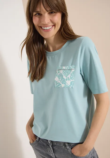 T-Shirt mit Rundhals und Brusttasche crystal mint Eine junge Frau trägt ein hellblaues T-Shirt mit kurzem Arm und gemustertem Brusttaschen-Print.