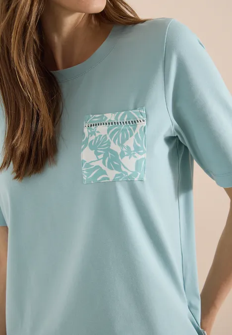 T-Shirt mit Rundhals und Brusttasche crystal mint Frau trägt hellblaues T-Shirt mit aufgesetzter Brusttasche in Weiß mit tropischem Blattmuster.