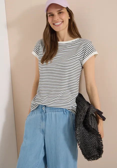 T-Shirt mit Boat Neck und Streifen palm breeze green Junge Frau trägt gestreiftes T-Shirt und lockere Jeanshose, hält eine schwarze Tasche.