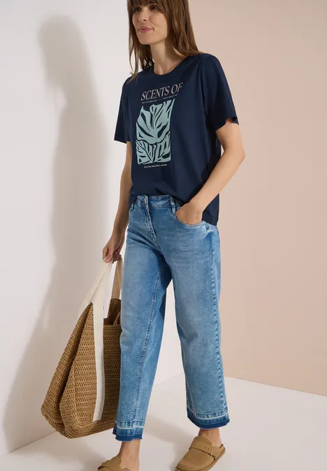 T-Shirt mit Rundhals und Frontprint universal blue Frau trägt dunkelblaues T-Shirt mit Aufdruck, lockere Jeans und eine große Basttasche.