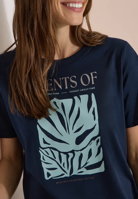 T-Shirt mit Rundhals und Frontprint universal blue Eine lächelnde Frau trägt ein dunkelblaues T-Shirt mit grünem abstraktem Blattmotiv.