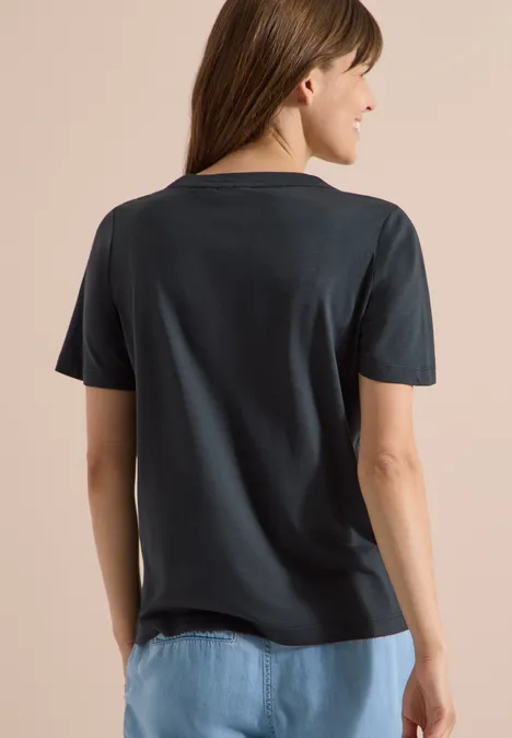 T-Shirt mit Rundhals und Frontprint palm breeze green Rückansicht einer Frau mit dunkelgrauem T-Shirt und hellblauen Jeans.
