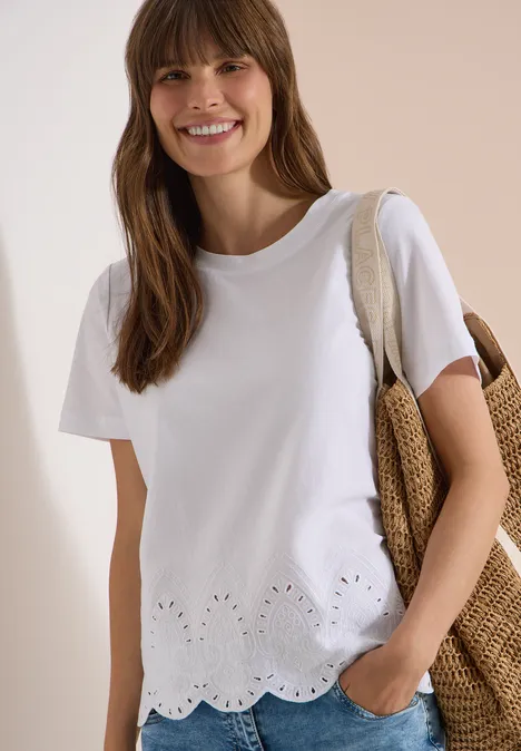 Weißes T-Shirt mit gewelltem, gesticktem Saum, kombiniert mit einer geflochtenen Strohtasche