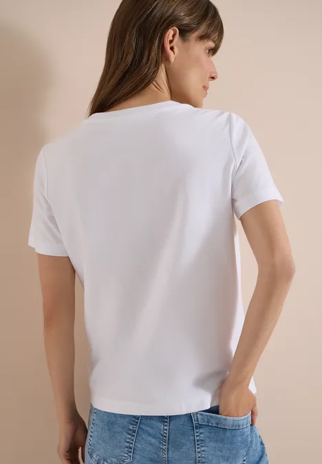 Frau von hinten in weißem T-Shirt und Jeans vor neutralem Hintergrund.
