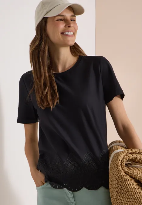 Vrouw in zwart t-shirt met gegolfde zoom, houdt strozak vast tegen lichte achtergrond.