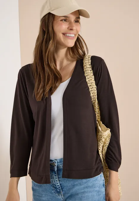 Vrouw met beige pet draagt een zwarte cardigan, een wit topje en een rieten tas.