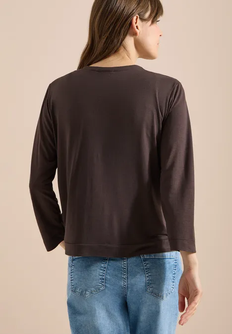 Vrouw van achteren in een zwart shirt met lange mouwen en blauwe jeans voor een lichte achtergrond.