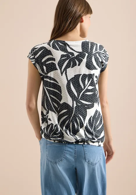 T-Shirt in Ausbrenner-Optik palm breeze green Rückansicht einer Frau in weißem Shirt mit schwarzem Blattmuster und hellblauen Jeans.