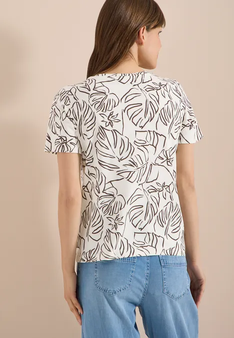 Vrouw van achteren in wit T-shirt met bruin bladmotief en blauwe spijkerbroek.