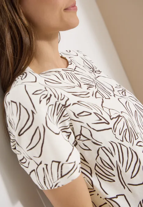 Close-up van een vrouw in een wit T-shirt met zwart bladerpatroon.