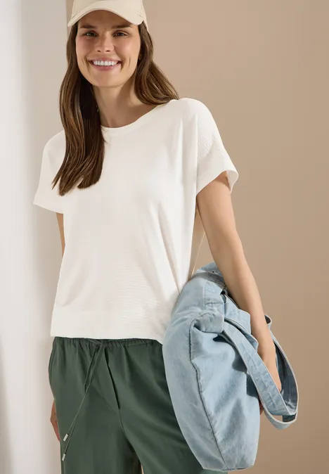 Frau in weißem T-Shirt und grüner Hose hält eine große hellblaue Tasche.
