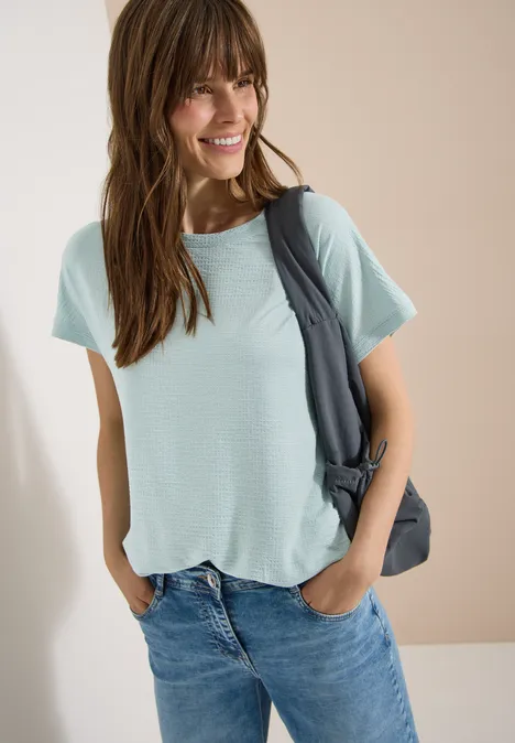 Shirt met ronde hals en structuur crystal mint Vrouw met lichtblauw T-shirt, blauwe spijkerbroek en een donkergrijze tas over de schouder.
