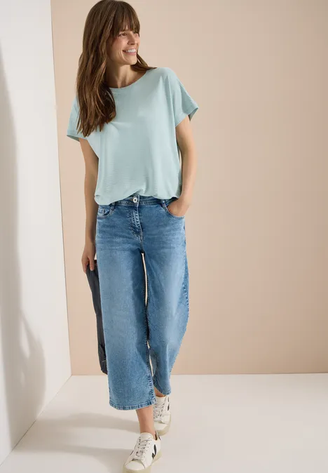 Shirt met ronde hals en structuur crystal mint Vrouw in mintgroen T-shirt en wijde cropped jeans glimlachend voor een beige achtergrond.