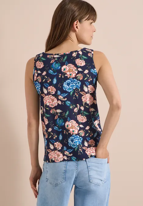 Frau von hinten in dunkelblauem ärmellosem Top mit buntem Blumenmuster und heller Jeans.