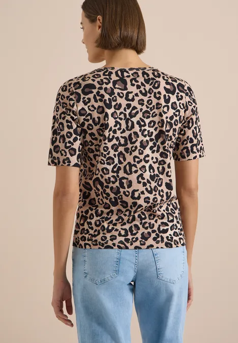 Frau von hinten in Jeans und kurzärmeligem, beigem T-Shirt mit schwarzem Leopardenmuster.