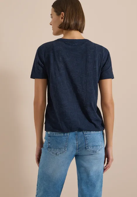 T-Shirt in Ausbrenner-Optik universal blue Eine Person von hinten in dunkelblauem T-Shirt und blauen Jeans vor beigem Hintergrund.