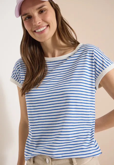T-Shirt mit Boat Neck und Streifen surf blue Frau im blau-weiß gestreiften T-Shirt mit kurzen Ärmeln vor hellem Hintergrund, Oberkörper sichtbar.
