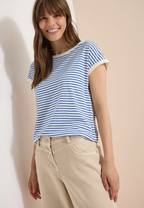 T-Shirt mit Boat Neck und Streifen surf blue Frau trägt blau-weiß gestreiftes T-Shirt und beige Hose vor hellem Hintergrund.