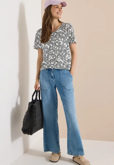 Vrouw in print-t-shirt, wijde jeans, pet en gevlochten tas