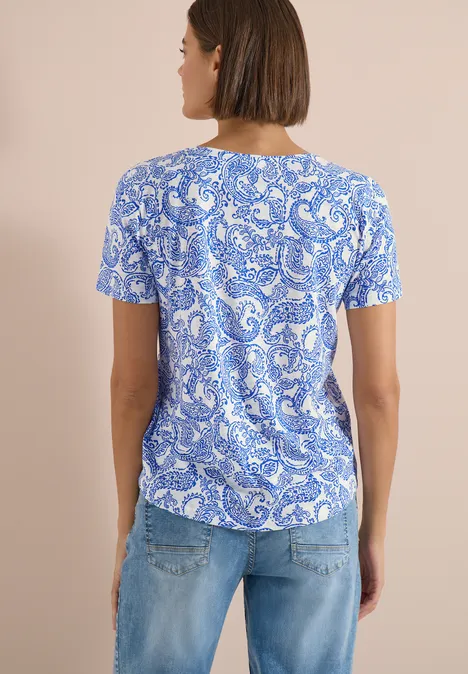 Achteraanzicht van een vrouw met blauw-wit gemêleerd T-shirt en lichtblauwe jeans voor een beige achtergrond.