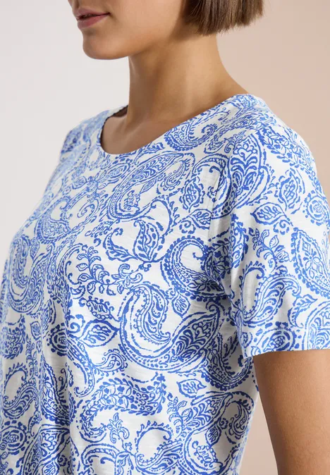 Vrouw in profiel met wit T-shirt met blauwe paisleyprint.