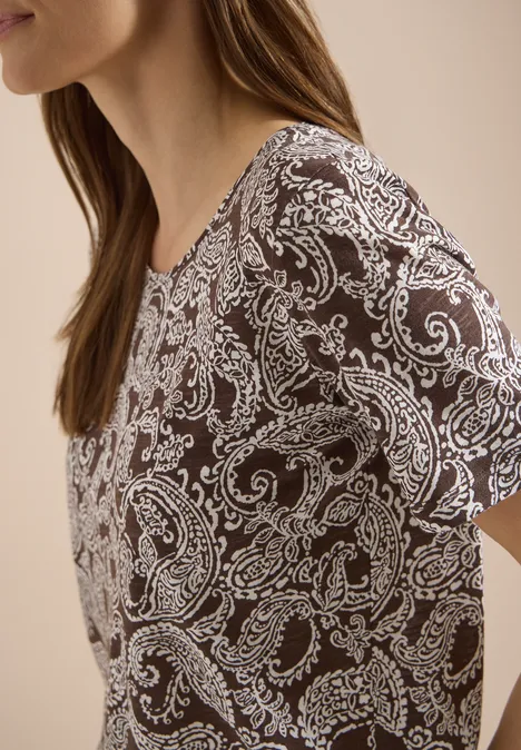 Seitenansicht einer Frau in einem dunkelbraunen Oberteil mit weißem Paisley-Muster