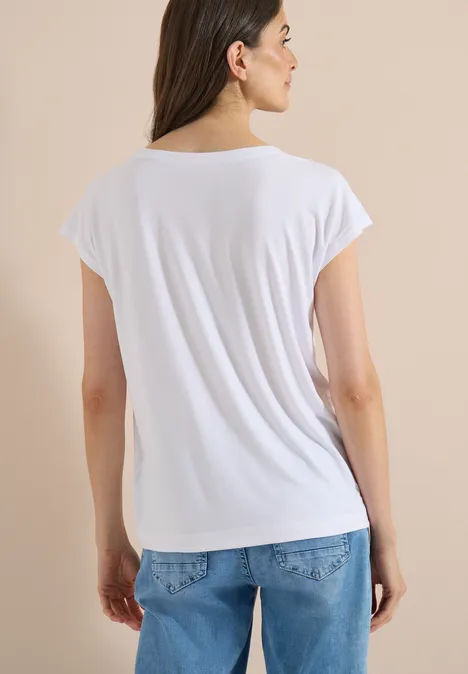 Persoon van achteren in een wit T-shirt en blauwe spijkerbroek tegen beige achtergrond.