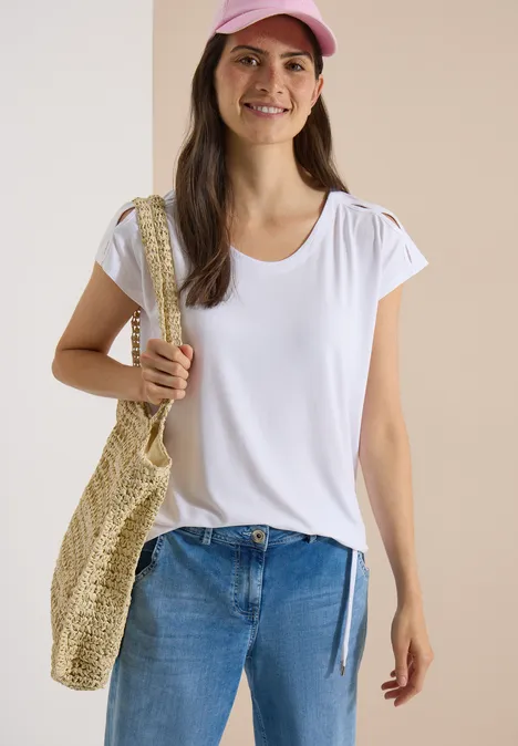 Vrouw in wit T-shirt, blauwe jeans en roze pet, met een rieten tas.