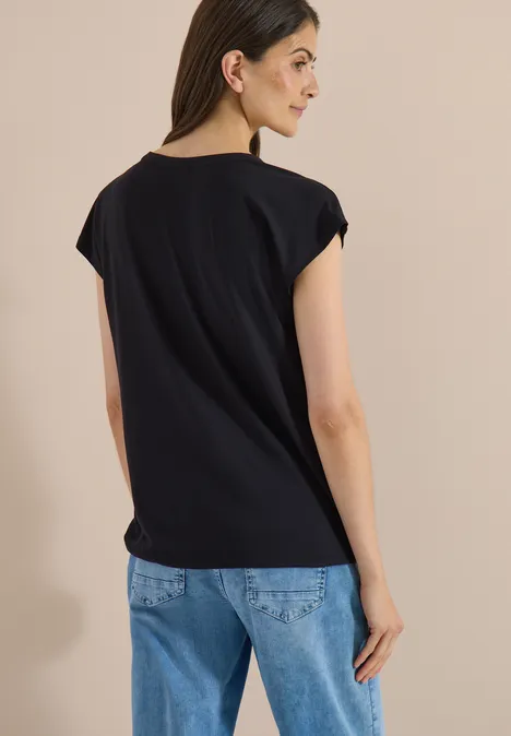 Achteraanzicht van een vrouw in een zwart t-shirt en blauwe jeans tegen een neutrale achtergrond.