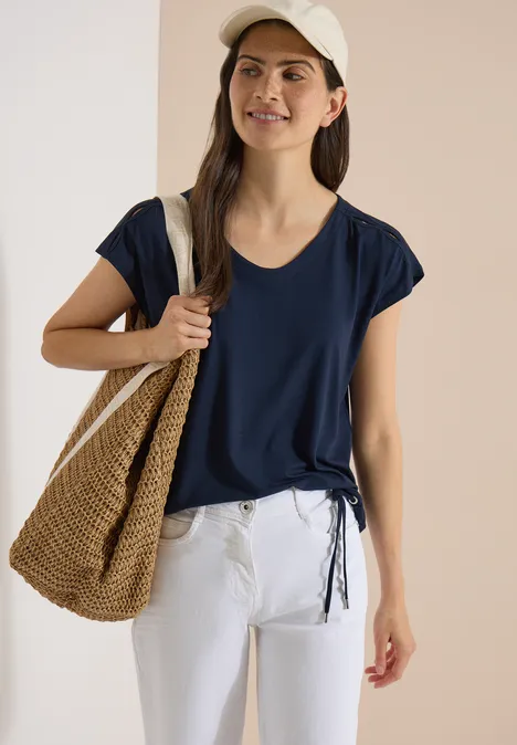 Vrouw in donkerblauw shirt, witte broek, strooien tas en pet