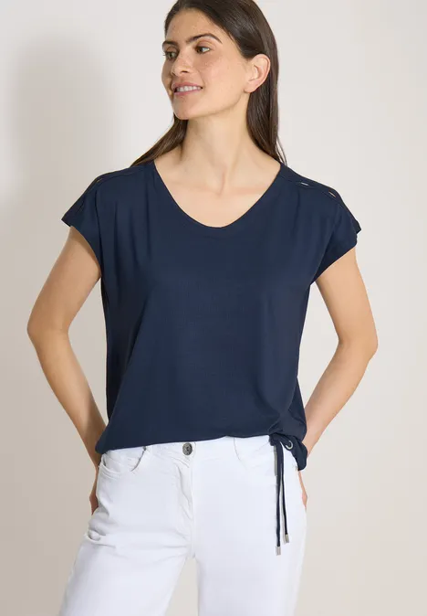 Vrouw in donkerblauw T-shirt met korte mouwen en witte broek.