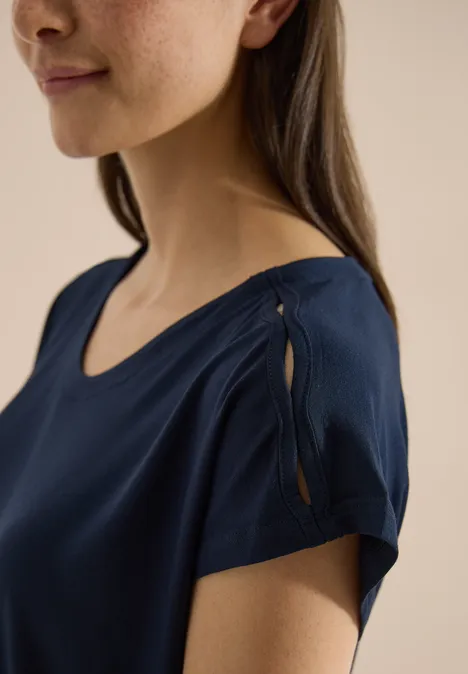 Een vrouw in een donkerblauw, kort mouw shirt met een split en knoopdetail op de schouder.