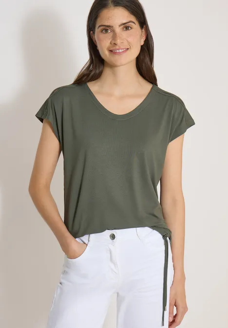 Frau in olivgrünem T-Shirt mit kurzen Ärmeln und weißer Hose.