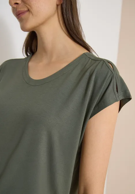 Eine Frau trägt ein khakifarbenes T-Shirt mit Cut-out-Detail an der Schulter.