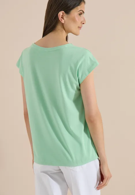 Vrouw van achteren in mintgroen t-shirt en witte broek voor neutrale achtergrond.