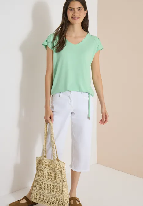 Vrouw in mintgroen t-shirt en witte culotte, met een gevlochten stroentas.