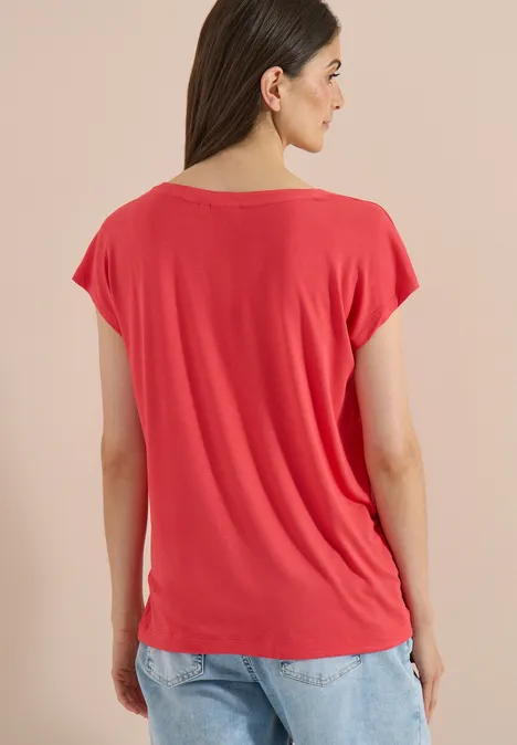 Vrouw van achteren in rood T-shirt met korte mouwen en blauwe jeans voor neutrale achtergrond.