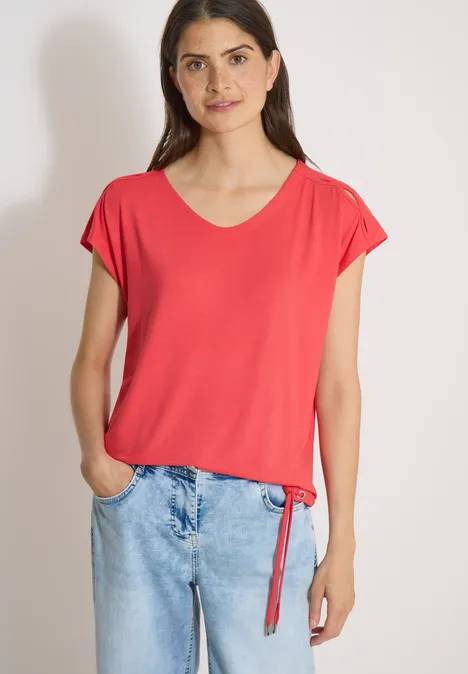 Vrouw in een rood t-shirt en losse spijkerbroek met handen in de zakken.