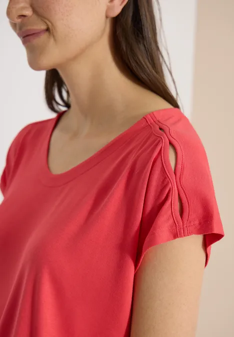 Vrouw in koraalrood shirt met ronde hals en sierlijke schouderopening