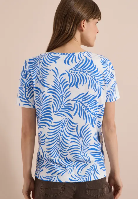 Achteraanzicht van een vrouw in een wit shirt met blauw bladmotief.