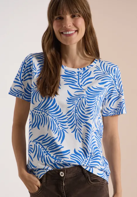 Vrouw in wit T-shirt met blauw palmbladerenpatroon, handen in de zakken