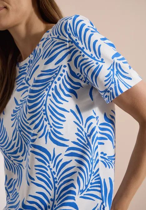 Wit T-shirt met blauw bladpatroon, model voor een neutrale achtergrond.