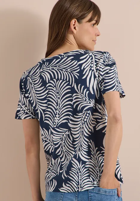 Vrouw van achteren in een donkerblauw t-shirt met wit bladpatroon.