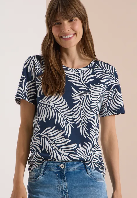 Vrouw draagt donkerblauw T-shirt met wit bladerenprint en spijkerbroek, gezicht onscherp.