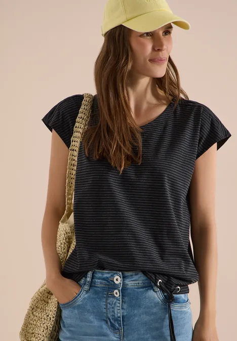 Frau in gestreiftem dunkelblauem T-Shirt, Jeans, Strohhut und Umhängetasche aus Bast.