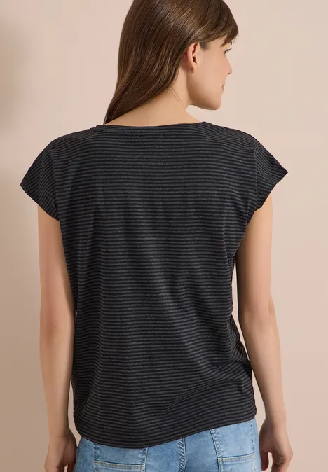 Frau von hinten in gestreiftem T-Shirt und Jeans vor hellem Hintergrund.
