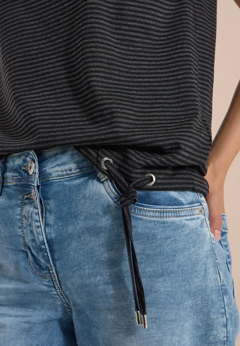 Hüftportrait in blauen Jeans mit Kordelzug und gestreiftem Oberteil, Hand in Tasche.